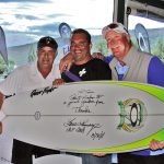 three men hold a signed oakley surfboard